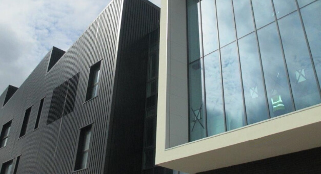 Modern building corner with dark vertical cladding and large glass window reflecting clouds, minimalist architectural style