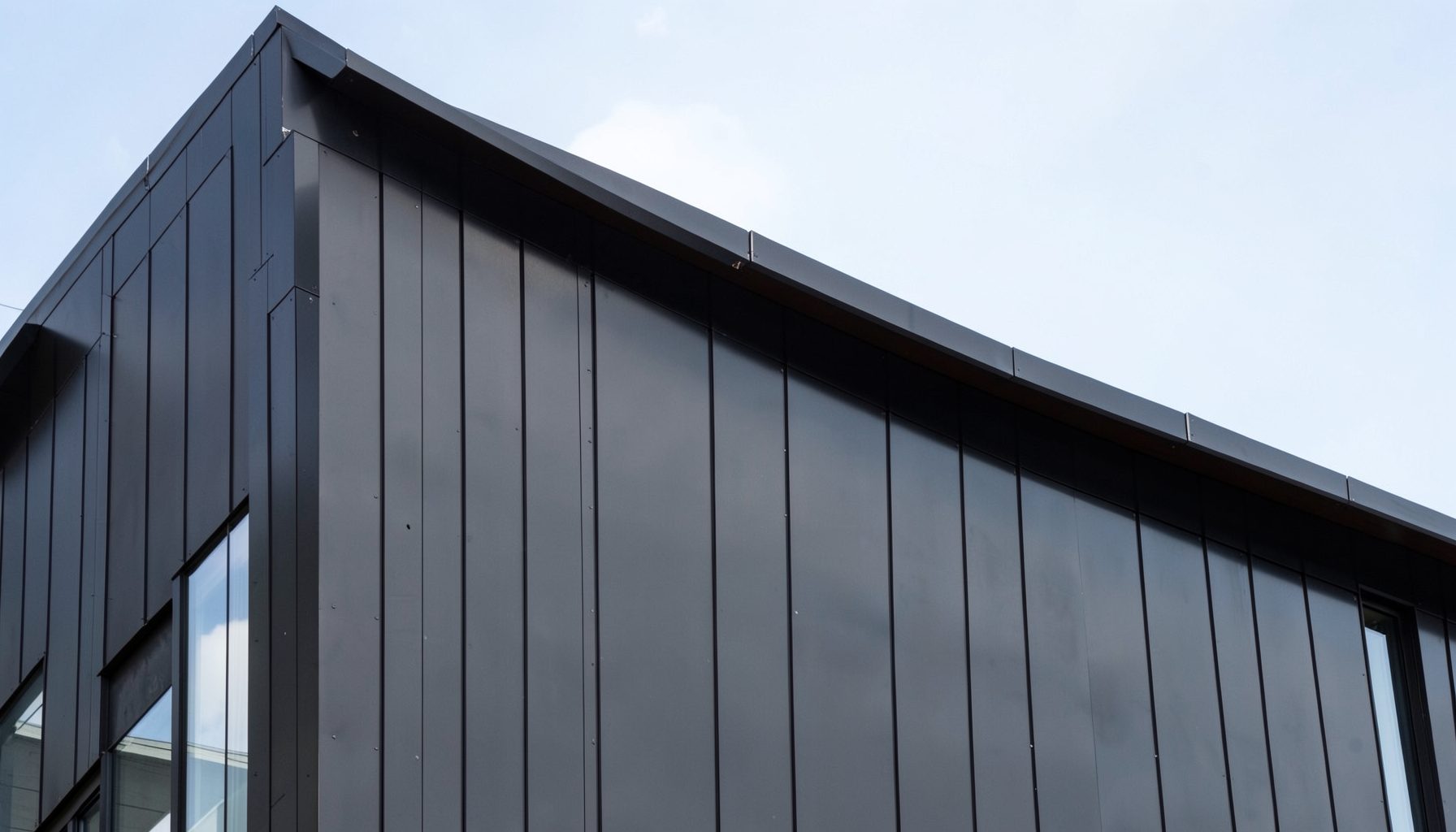 Modern building facade with dark metal cladding panels and clean architectural lines under a bright sky