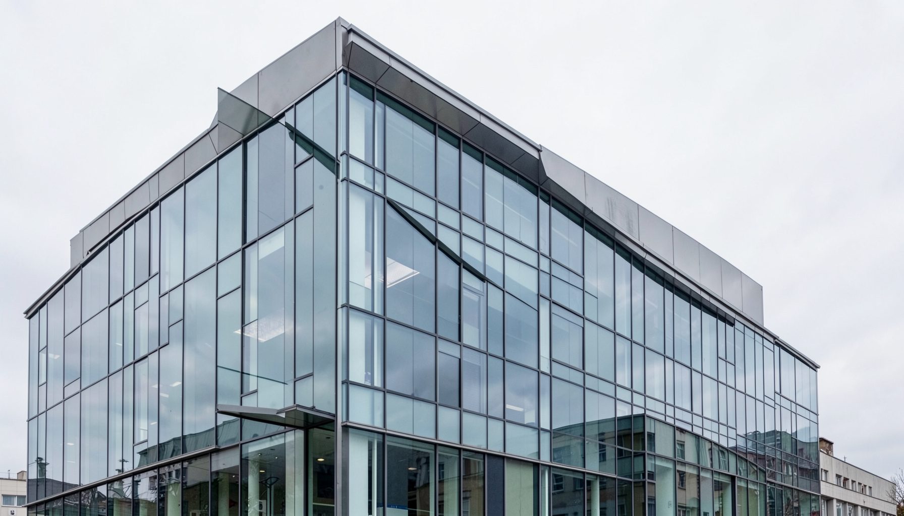 Modern glass and metal-clad building exterior with clean architectural lines, set against an overcast sky